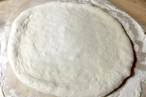 Pâte à pizza étalée sur une surface farinée, prête pour une recette pâte à pizza rapide.