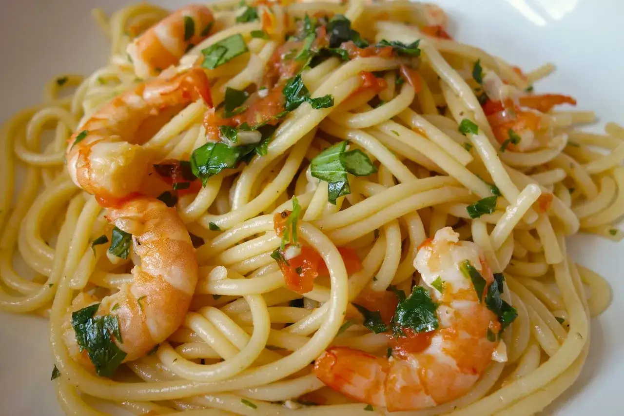 Un plat appétissant de spaghetti aux crevettes, garni de persil frais et de morceaux de tomates.