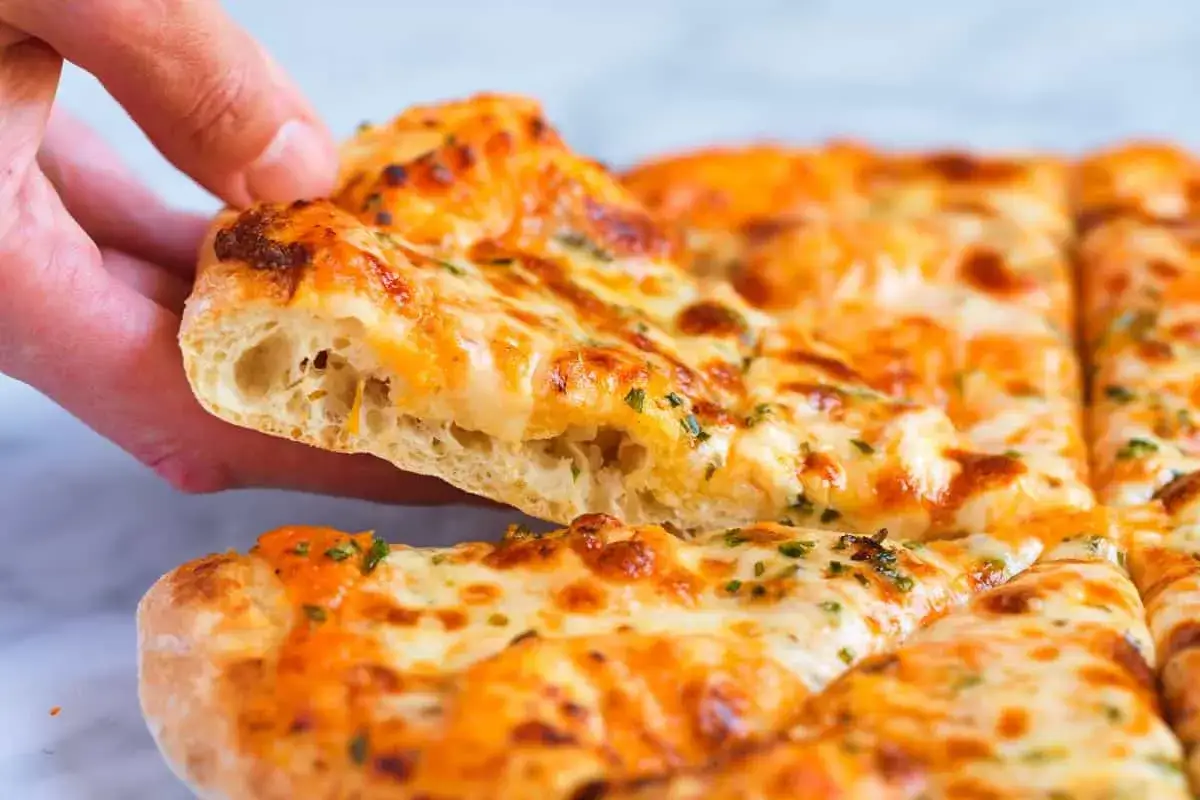 Une main soulève une part de pizza au fromage fondu, révélant la mie aérée de cette recette pâte à pizza moelleuse.