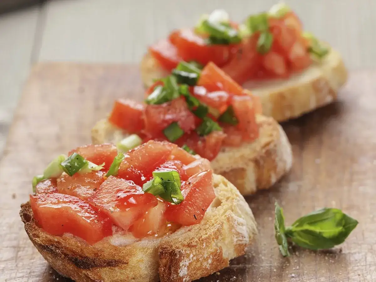 Trois délicieuses bruschettas garnies de tomates fraîches et d'oignons verts, parfaites pour une recette facile.