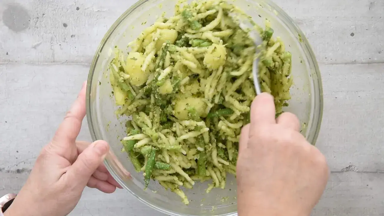 Un plat de pâtes italiennes avec des pommes de terre et des haricots verts, le tout enrobé d'une sauce verte.