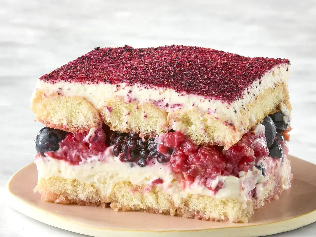 Tranche de tiramisu aux fruits rouges et myrtilles, saupoudrée de poudre de fruits.