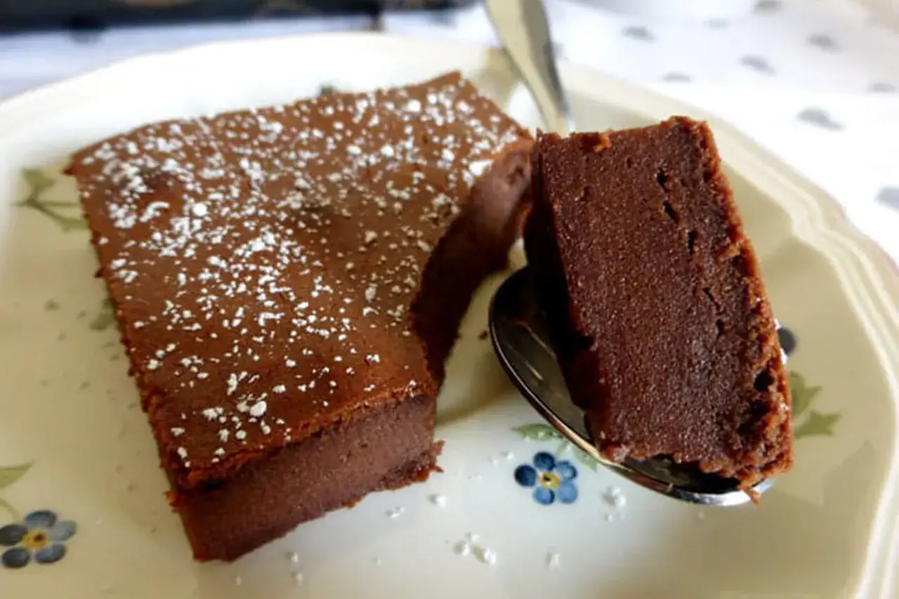 Un délicieux gâteau chocolat mascarpone facile, saupoudré de sucre glace, sur une assiette fleurie. Une part est prélevée à la cuillère.