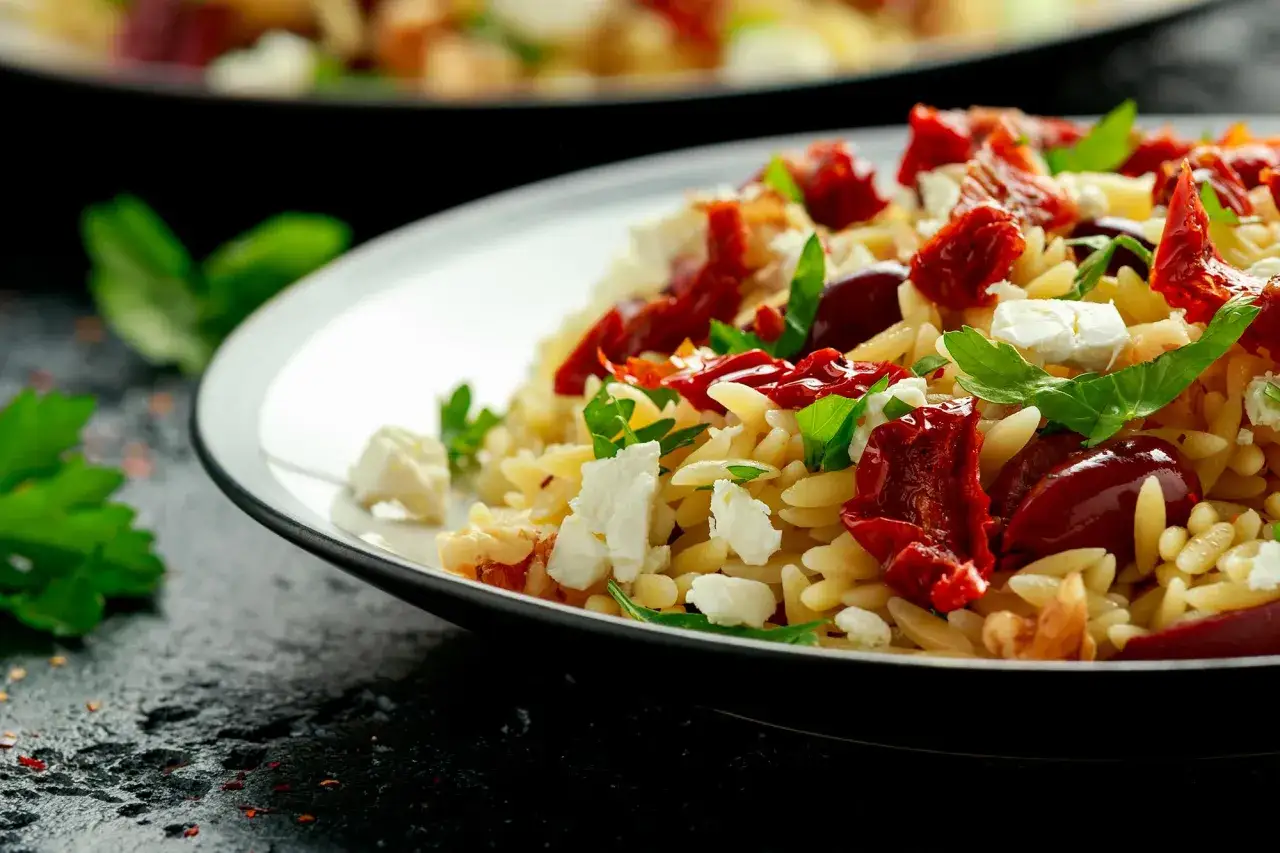 Salade de pâtes orzo avec tomates séchées, mozzarella fraîche, olives et basilic. Un plat coloré et savoureux.