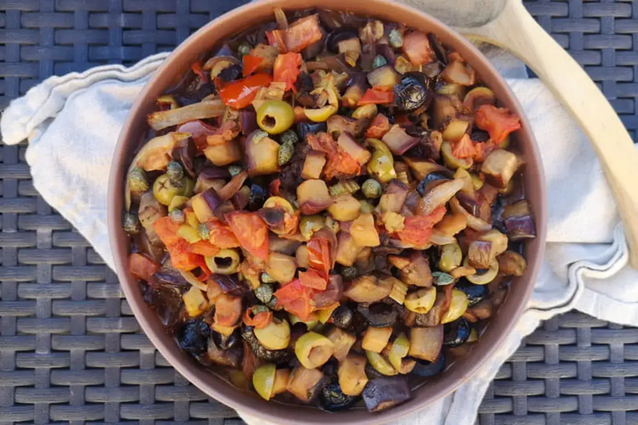 Un plat coloré de caponata sicilienne, mélange d'aubergines, tomates, olives et câpres, prêt à être dégusté.