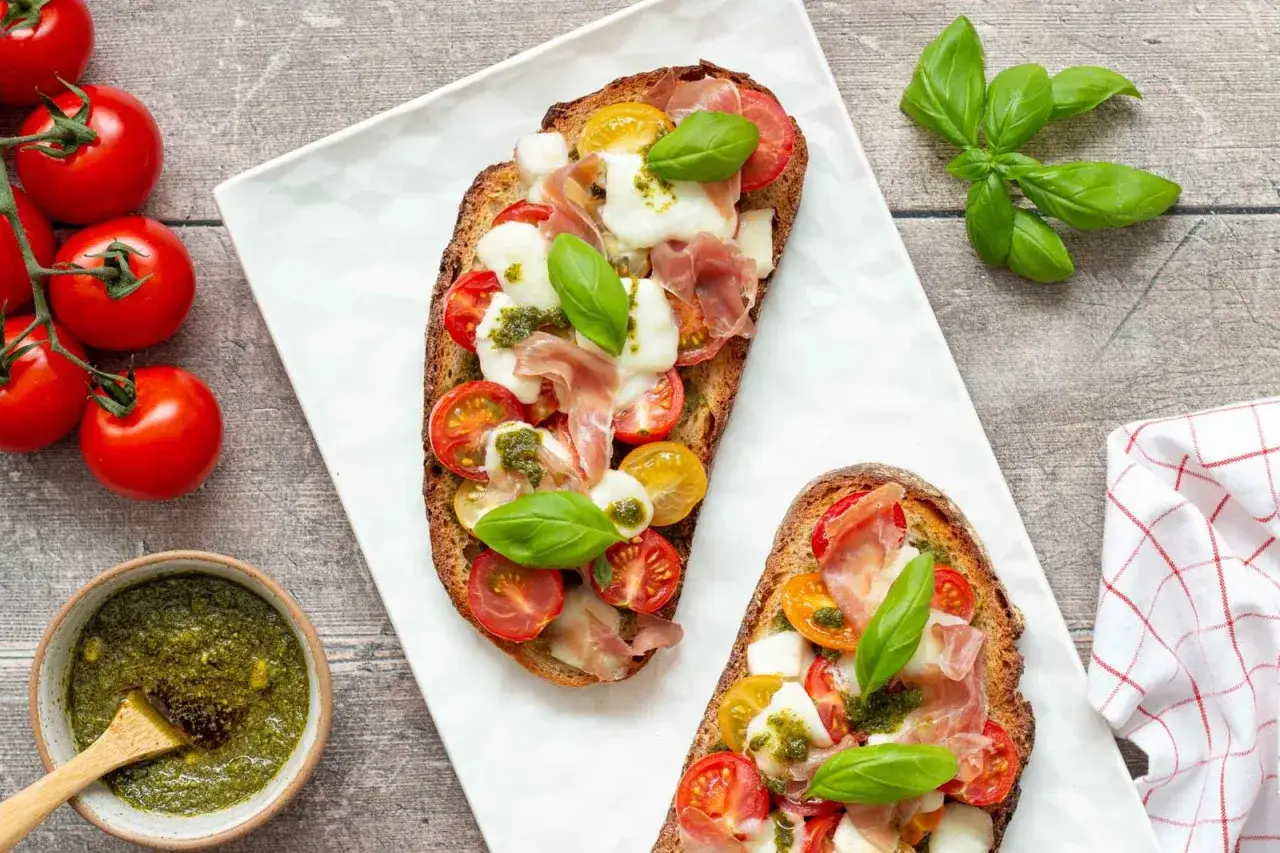 Deux bruschettas gourmandes garnies de tomates, mozzarella, jambon cru et d'un g&eacute;n&eacute;reux filet de pesto.