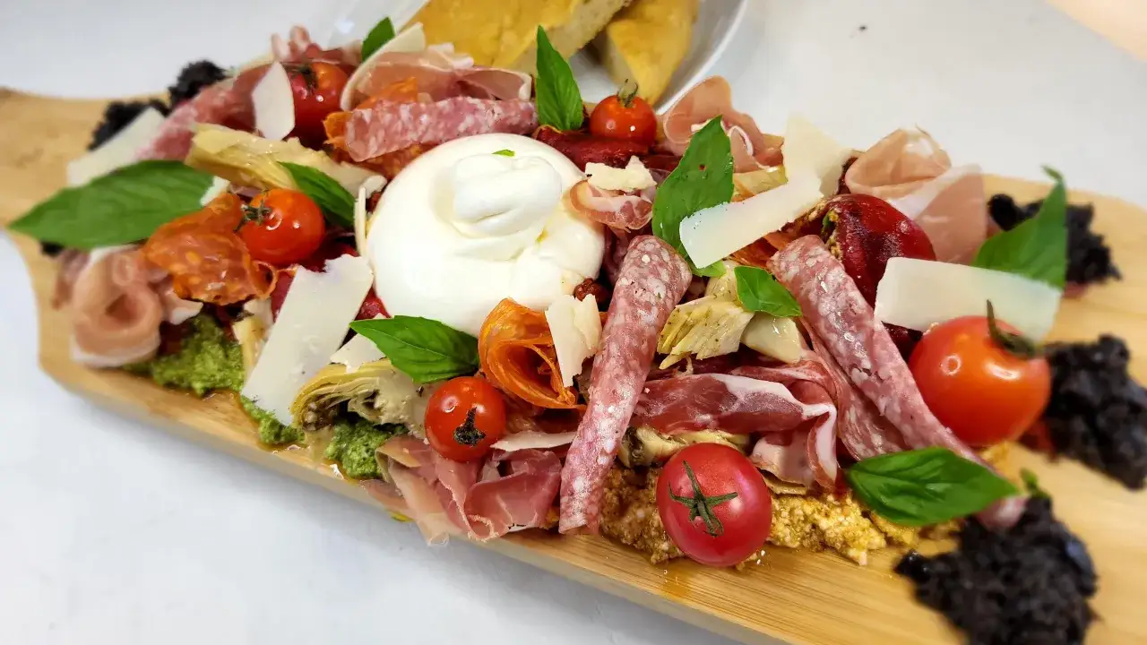 Plateau d'une entrée italienne : burrata crémeuse, charcuteries fines, tomates cerises, copeaux de parmesan et olives noires.