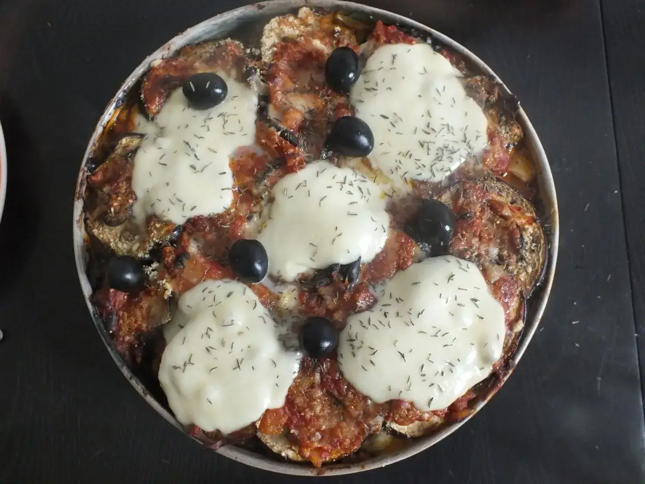 Un plat de recette aubergine mozzarella gratinée, avec des rondelles d'aubergine, sauce tomate, mozzarella fondue et olives noires.