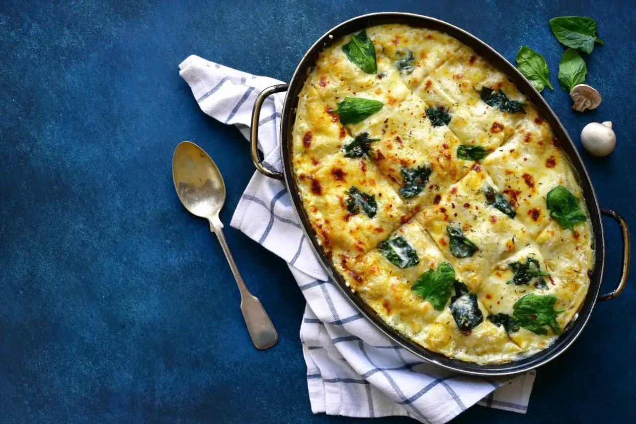 Lasagnes poulet champignons gratinées, garnies d'épinards frais et de fromage fondant, prêtes à être dégustées.