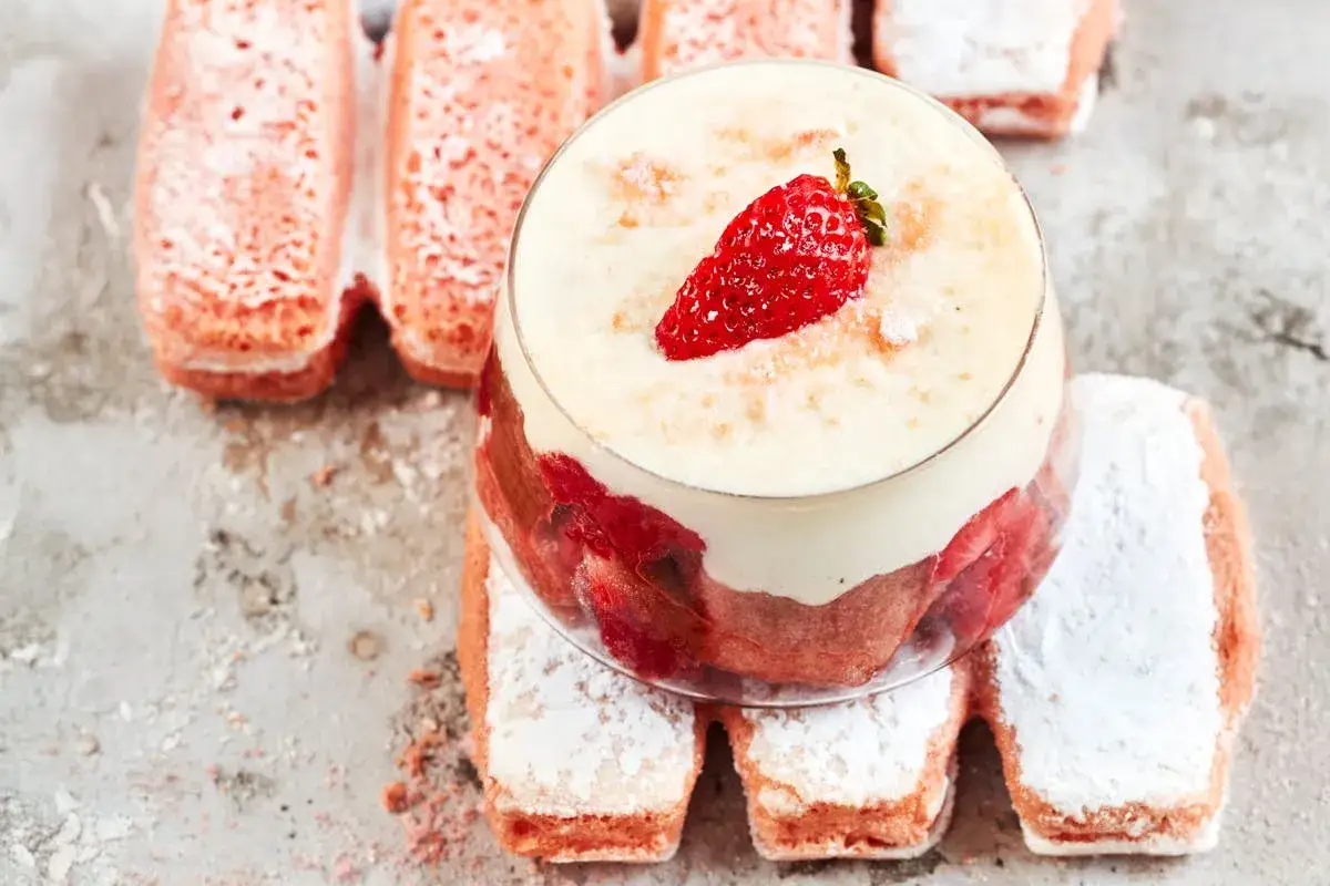 Un d&eacute;licieux tiramisu aux fraises, garni d'une fraise fra&icirc;che, entour&eacute; de biscuits roses saupoudr&eacute;s de sucre glace.
