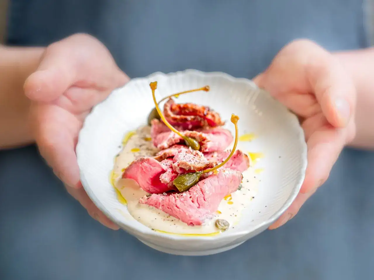 Fines tranches de vitello tonnato, nappées d'une sauce crémeuse et garnies de câpres, présentées dans une assiette blanche.