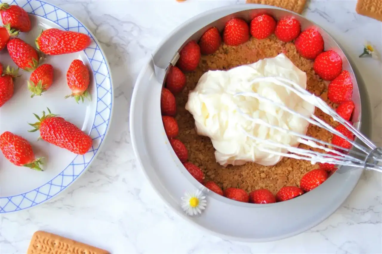Préparation d'une recette fraisier mascarpone : fraises fraîches, crème onctueuse et biscuits émiettés dans un cercle à pâtisserie.