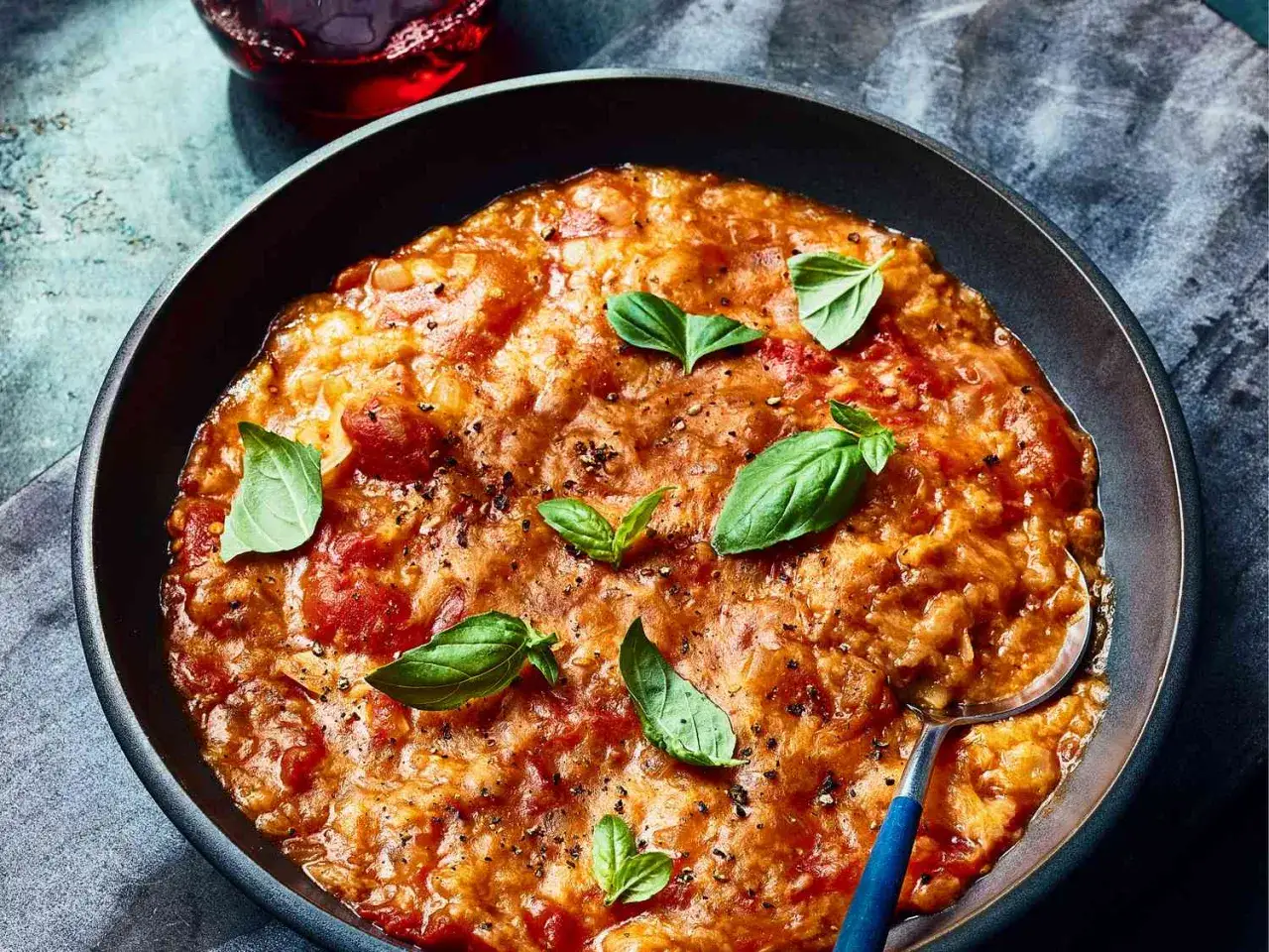 Un plat r&eacute;confortant de pappa al pomodoro, garni de feuilles de basilic frais et de poivre noir, servi dans un bol sombre.