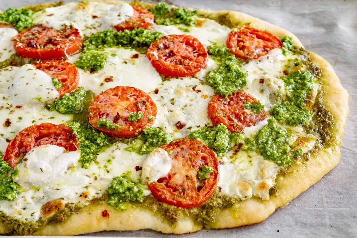 Pizza pesto avec tomates fraîches et mozzarella fondue, un délice coloré et savoureux.