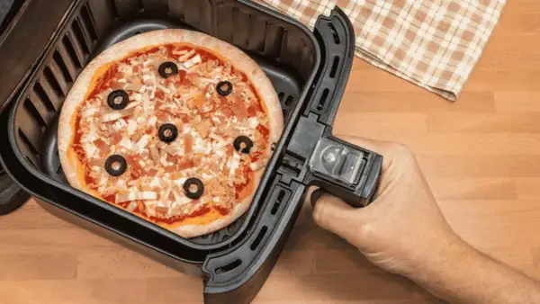 Une pizza garnie d'olives noires et de fromage est prête à être cuite dans un airfryer.